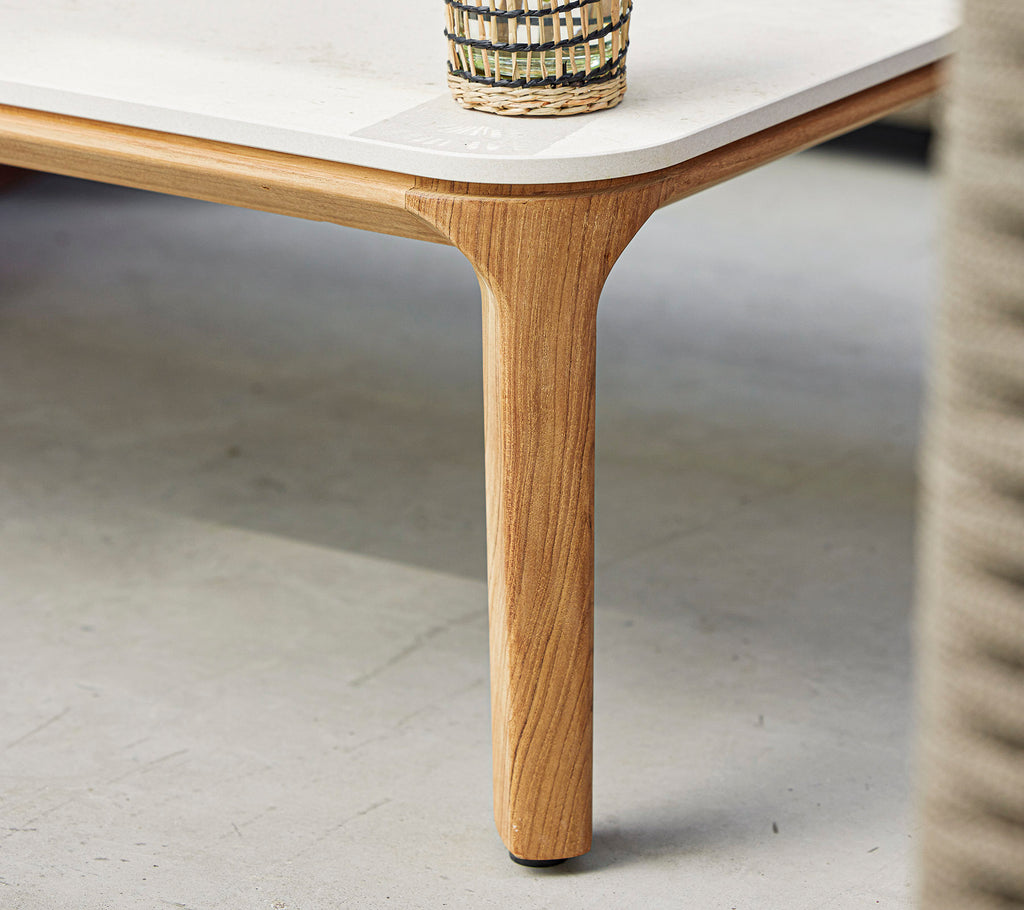 A stylish table featuring a smooth surface and a natural wood leg, topped with a decorative woven basket.
