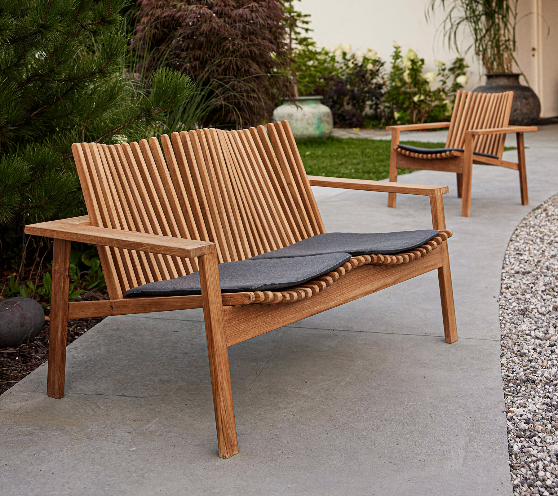 Modern wooden benches with slatted backrests and dark cushions, set in a landscaped area with greenery.
