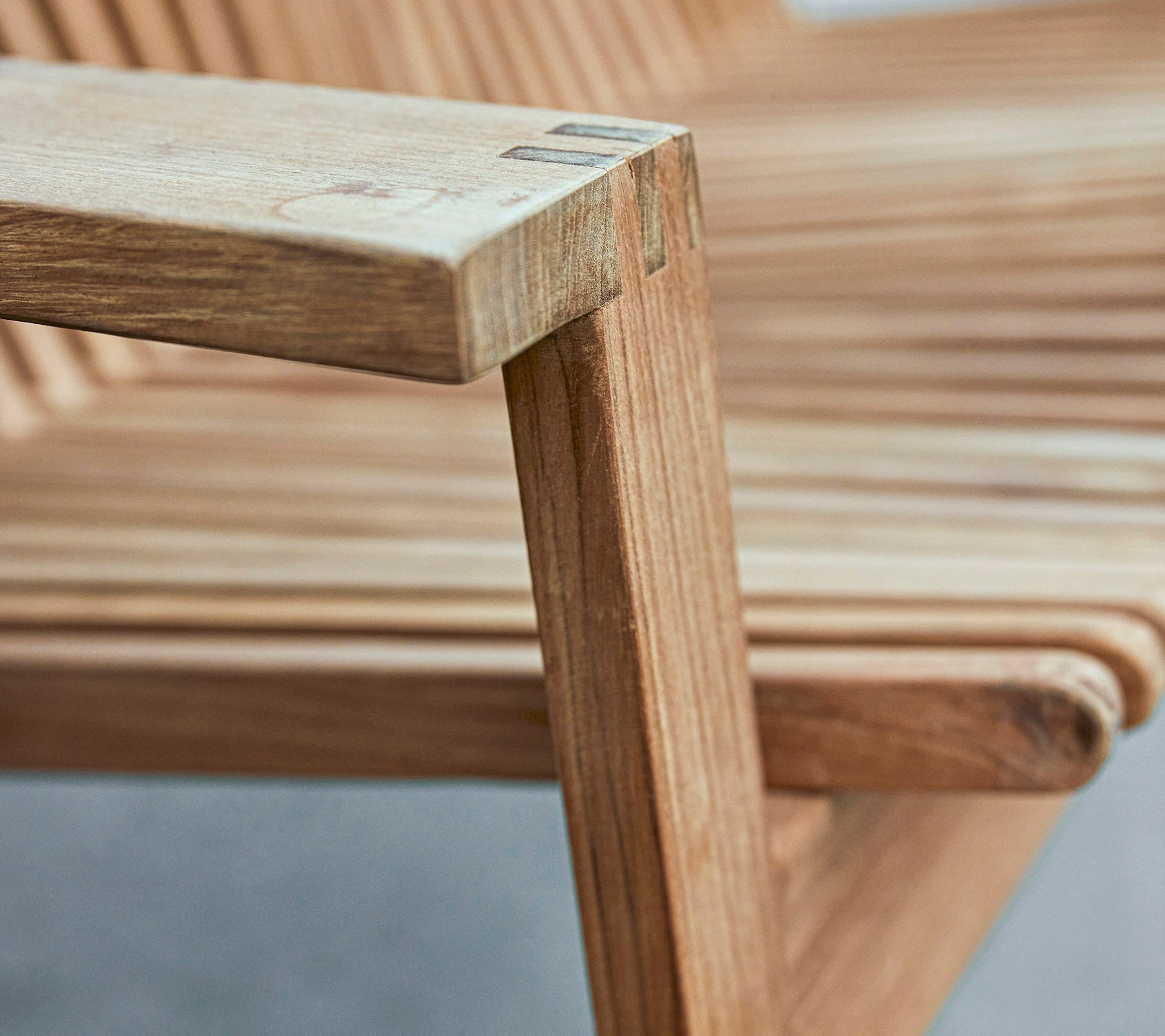 Close-up of a wooden chair armrest showcasing a sleek design with slatted seating and smooth finishes.
