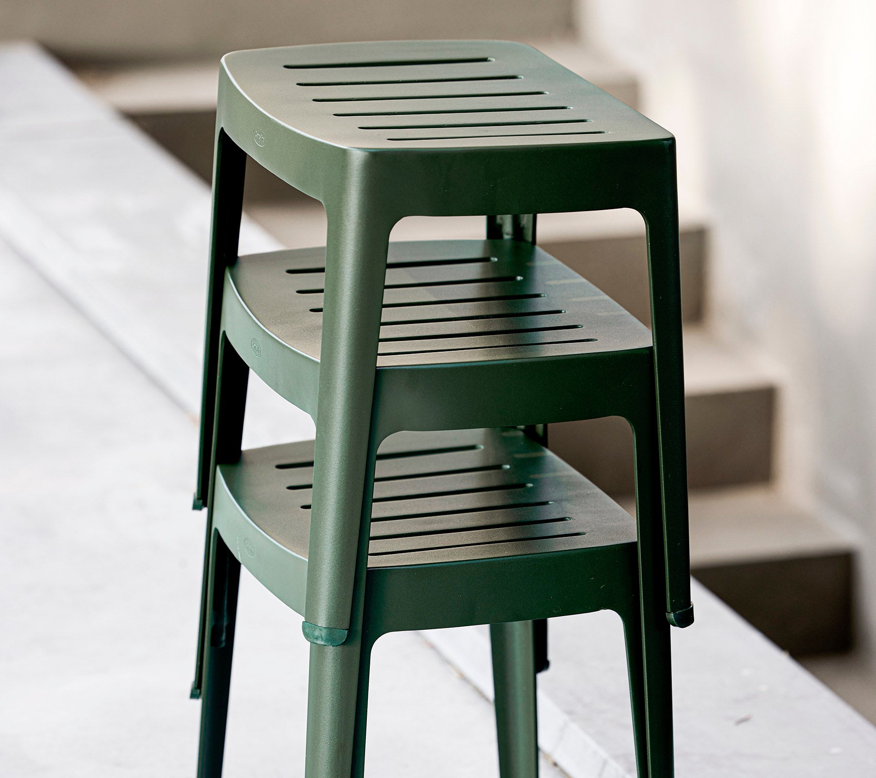 Stacked green plastic stools with slotted seats, designed for casual use. Ideal for versatile seating arrangements.