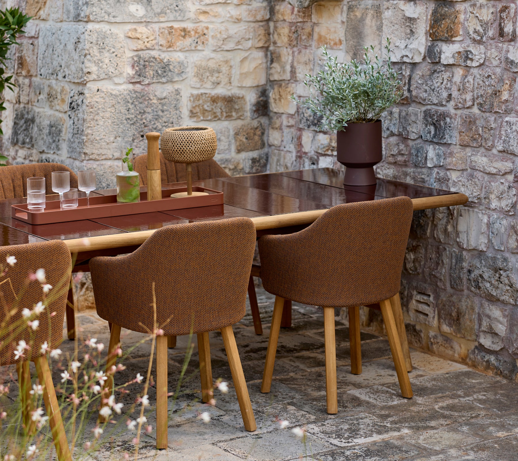 Brown chairs around a brown table with a decorative vase in an outdoor setting.