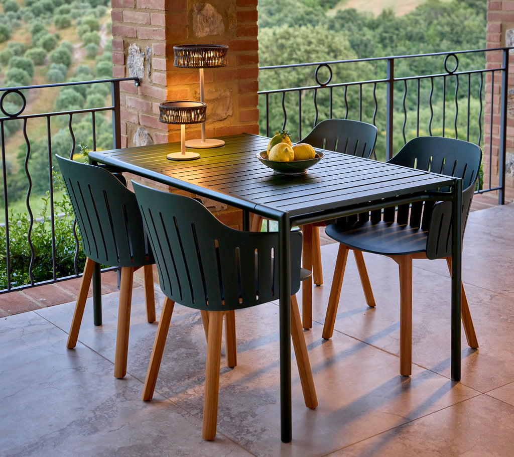 A stylish dining setup featuring a green rectangular table surrounded by black dining chairs, complemented by a fruit centerpiece and a lamp.