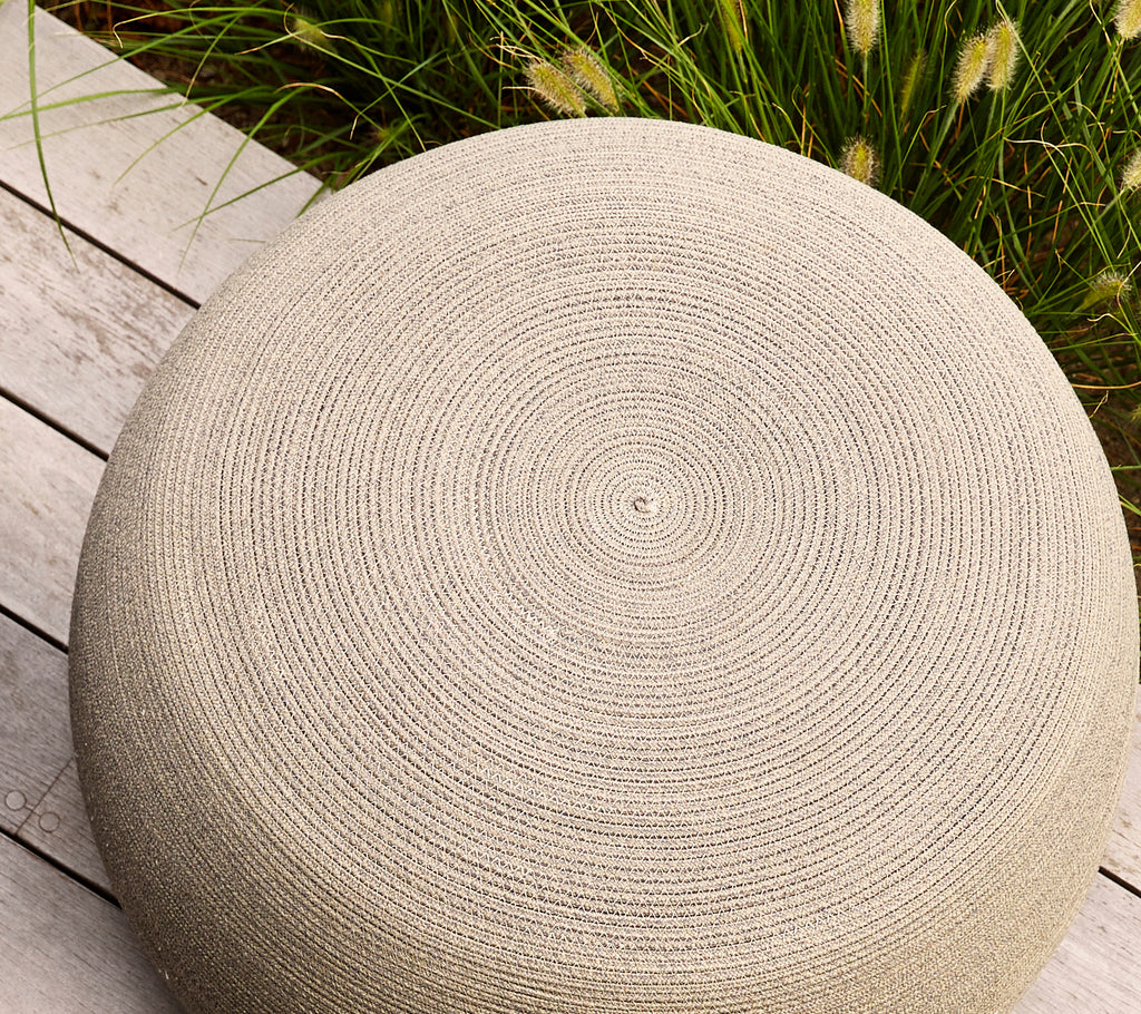Round taupe footstool with a textured surface featuring spiral patterns, ideal for versatile seating or decoration.