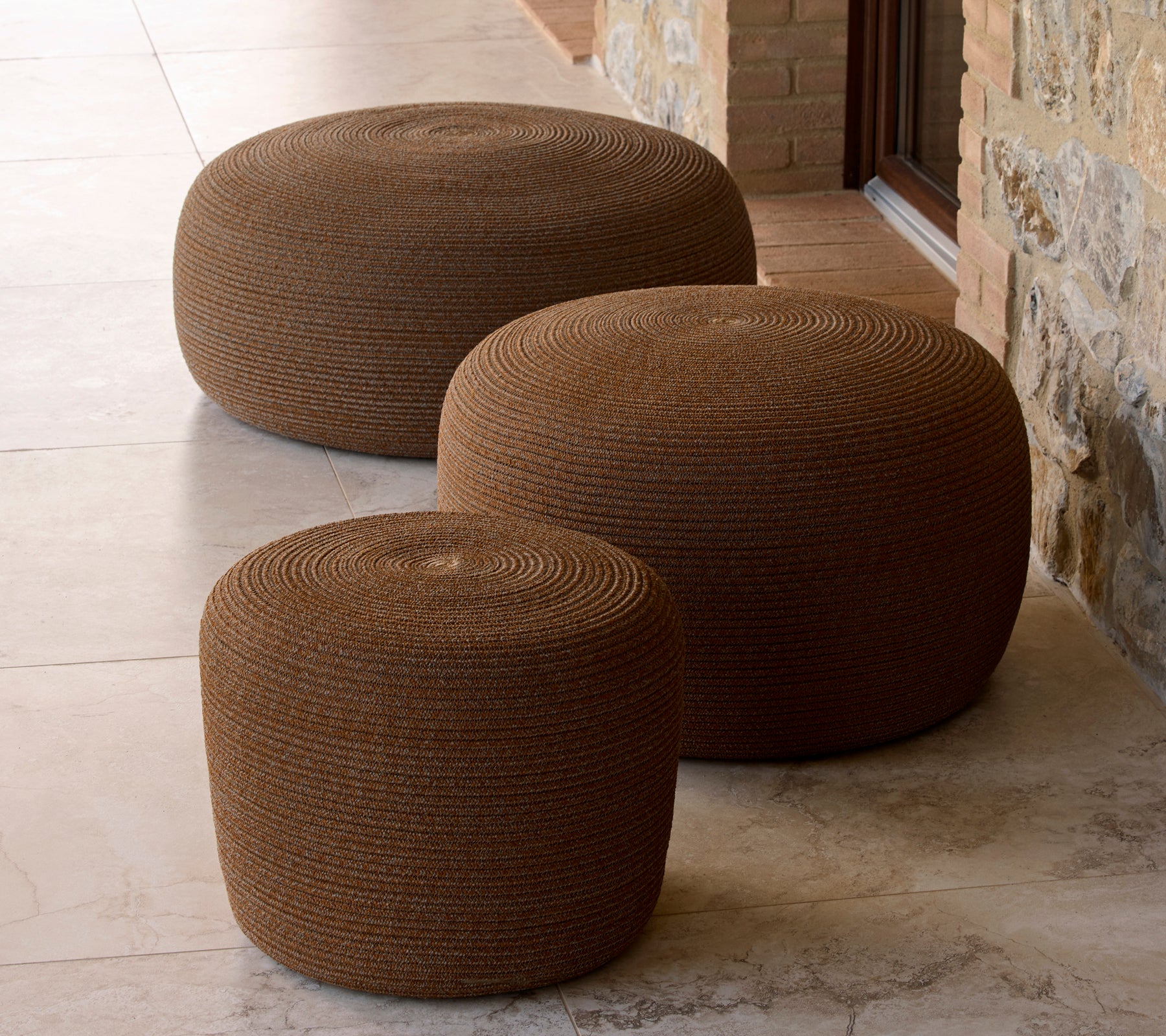 Three circular footstools in umber brown, varying in size, with a textured surface and round shape, arranged together.