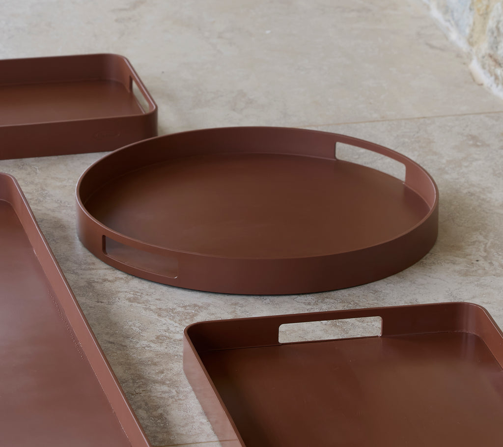 Round club tray in desert red, featuring a smooth surface and handles for easy carrying, alongside other trays in a similar style.