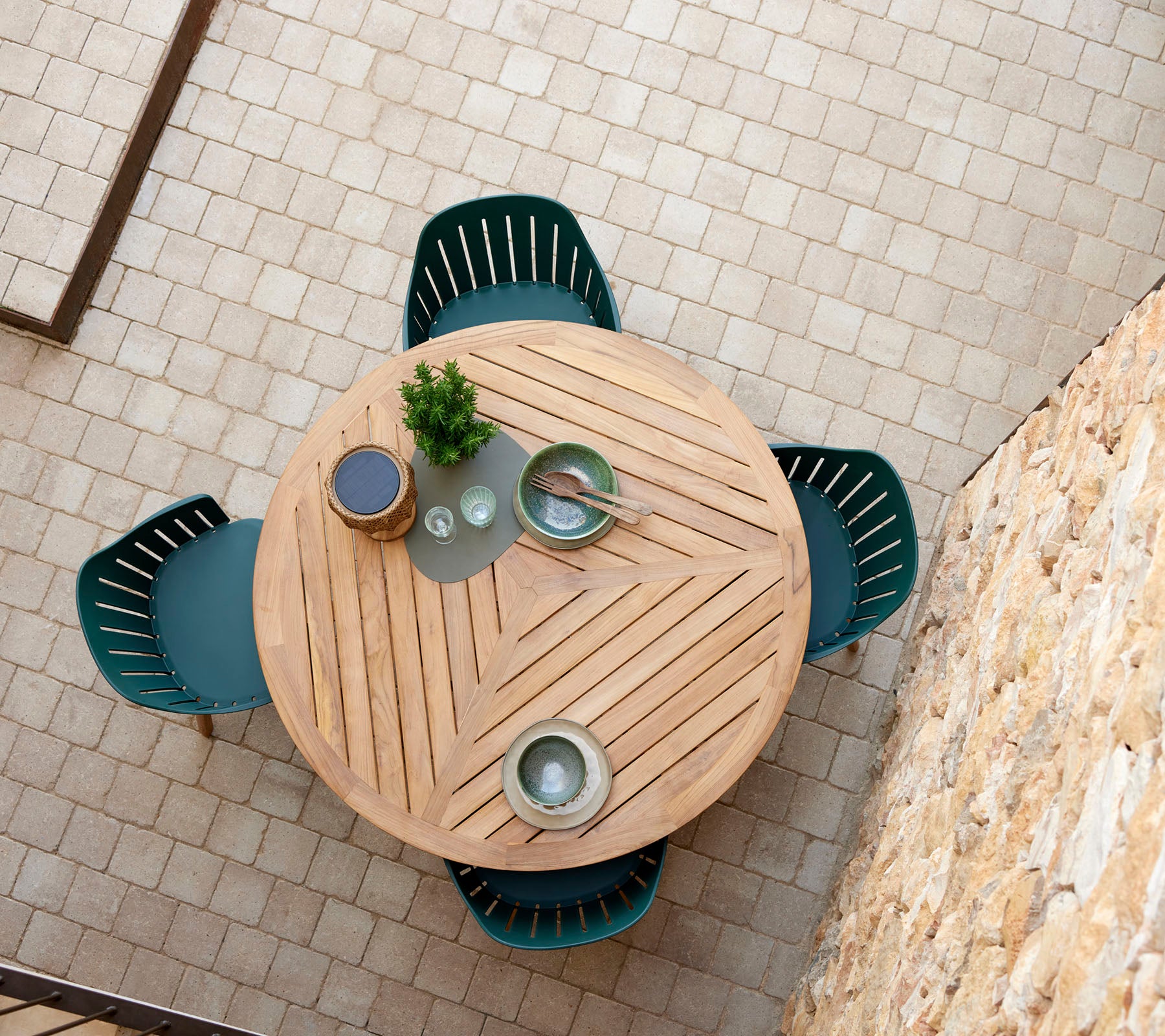 A round wooden table with a chevron pattern, surrounded by four green chairs, and adorned with decorative plates and a small plant.
