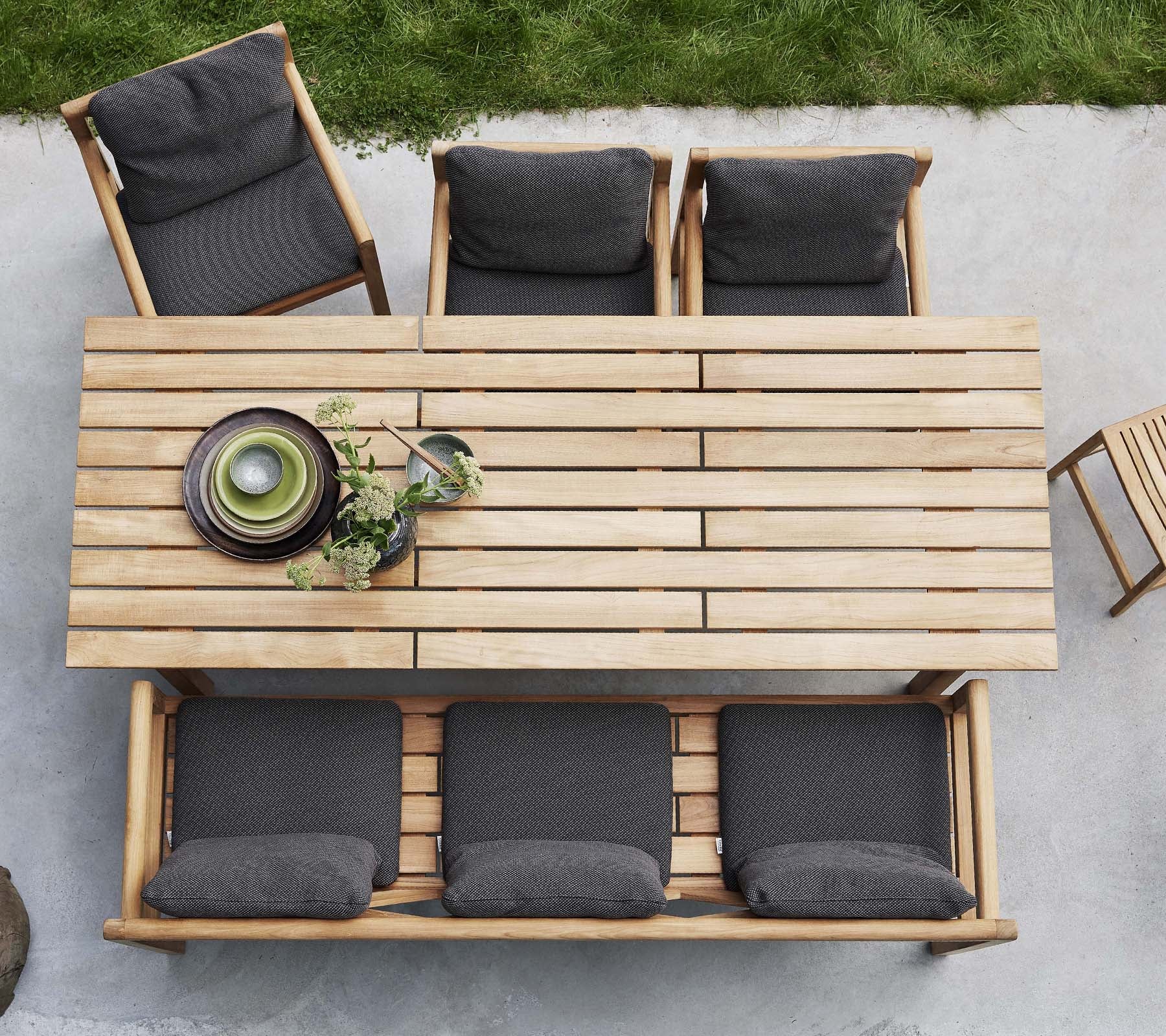 A wooden table accompanied by four chairs, each with dark cushions, featuring decorative plates and greenery on the table.