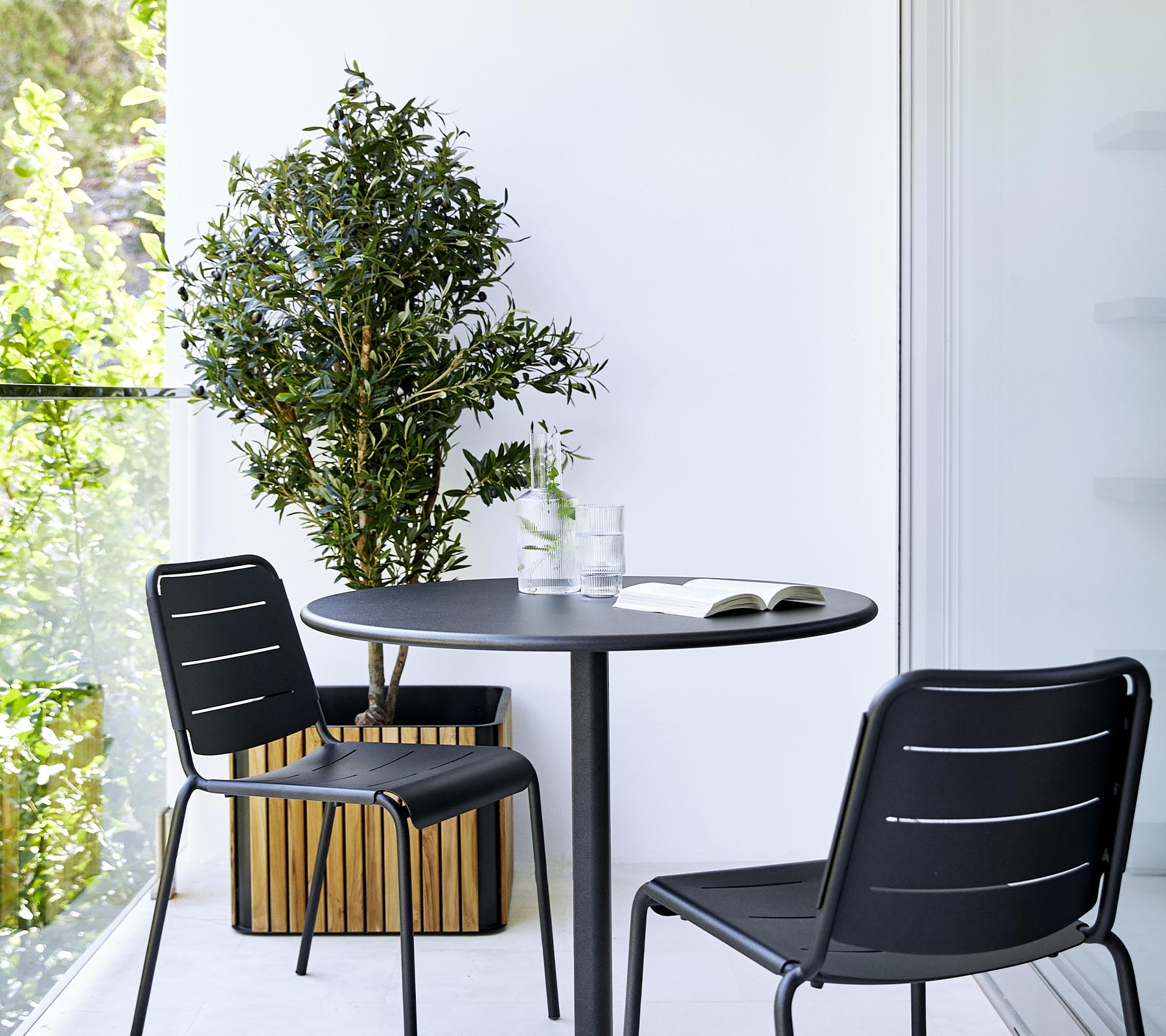 A modern dining setup featuring a round table, two black chairs, and a potted plant, creating a stylish and inviting atmosphere.