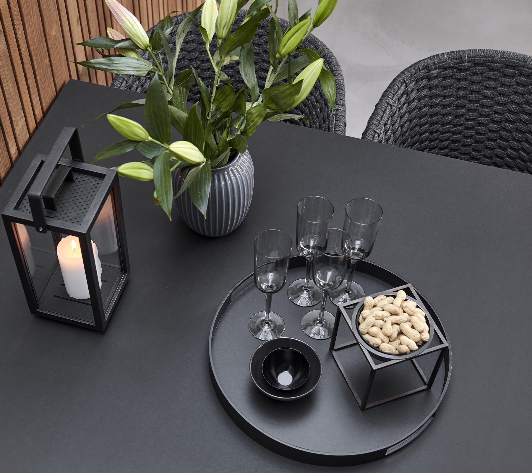 A stylish tabletop arrangement featuring a candle lantern, a vase with flowers, glasses, and a serving tray with snacks.