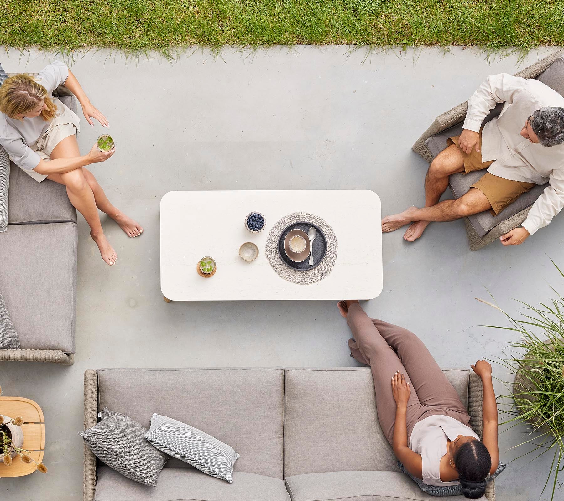 Aerial view of three people sitting around a coffee table with drinks, enjoying a relaxed gathering in a casual setting.