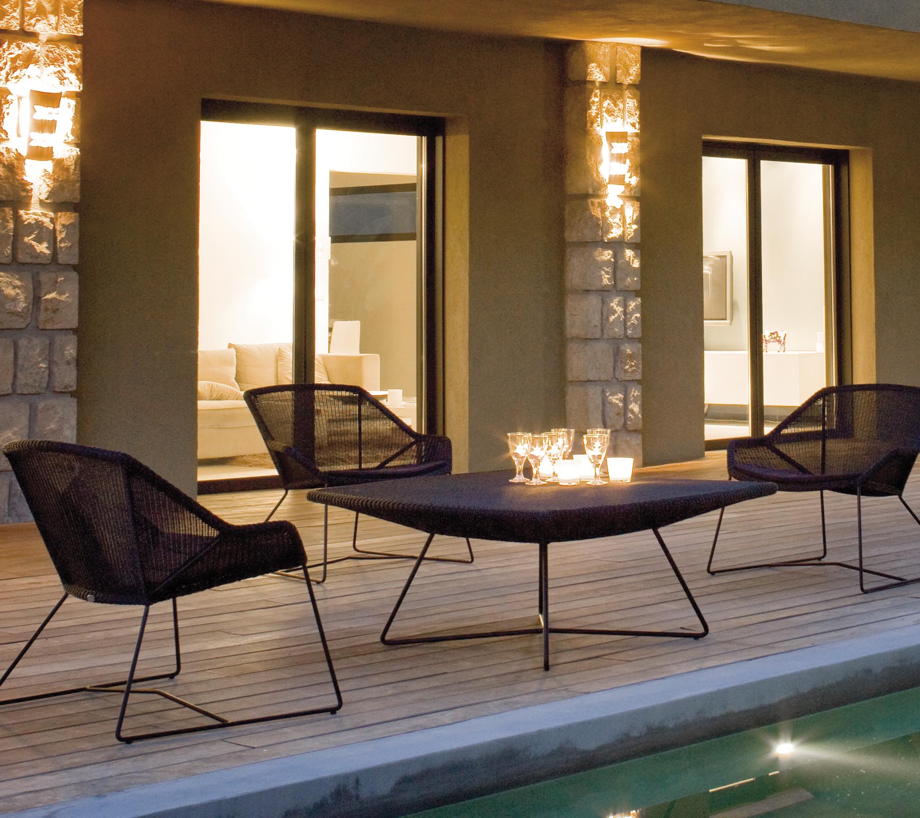 A stylish lounge seating arrangement featuring four black mesh chairs around a sleek table, illuminated by soft ambient lighting.