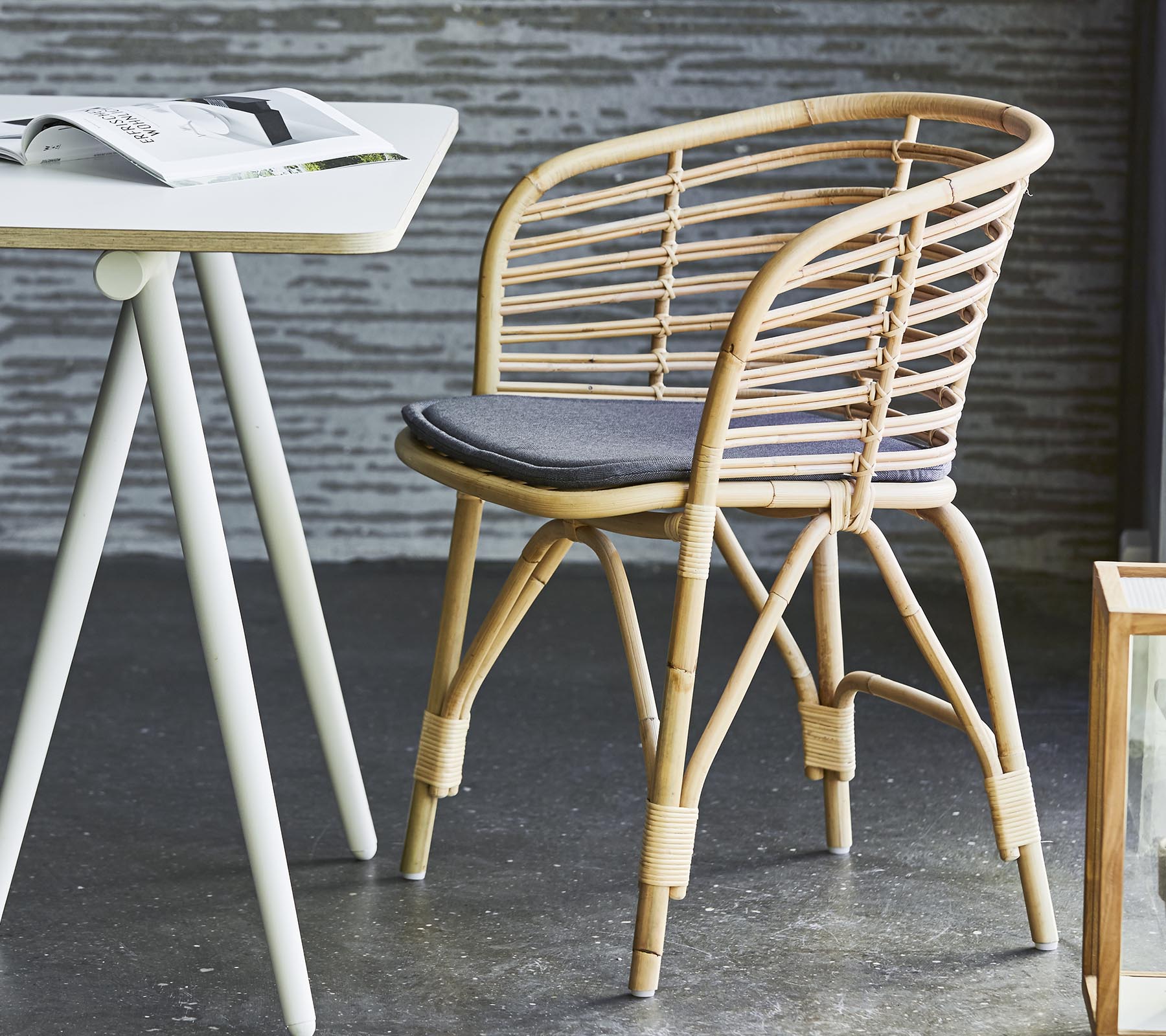 Stylish wicker chair with a gray cushion, paired with a simple table and contemporary decor. Suitable for casual seating and relaxation.