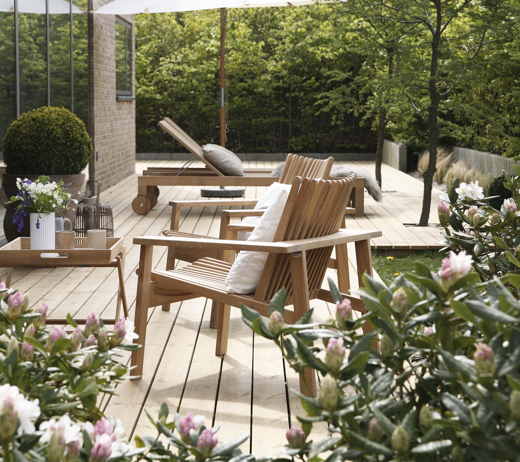 Wooden chairs and a table are surrounded by greenery and flowers, creating a serene and inviting outdoor seating area.