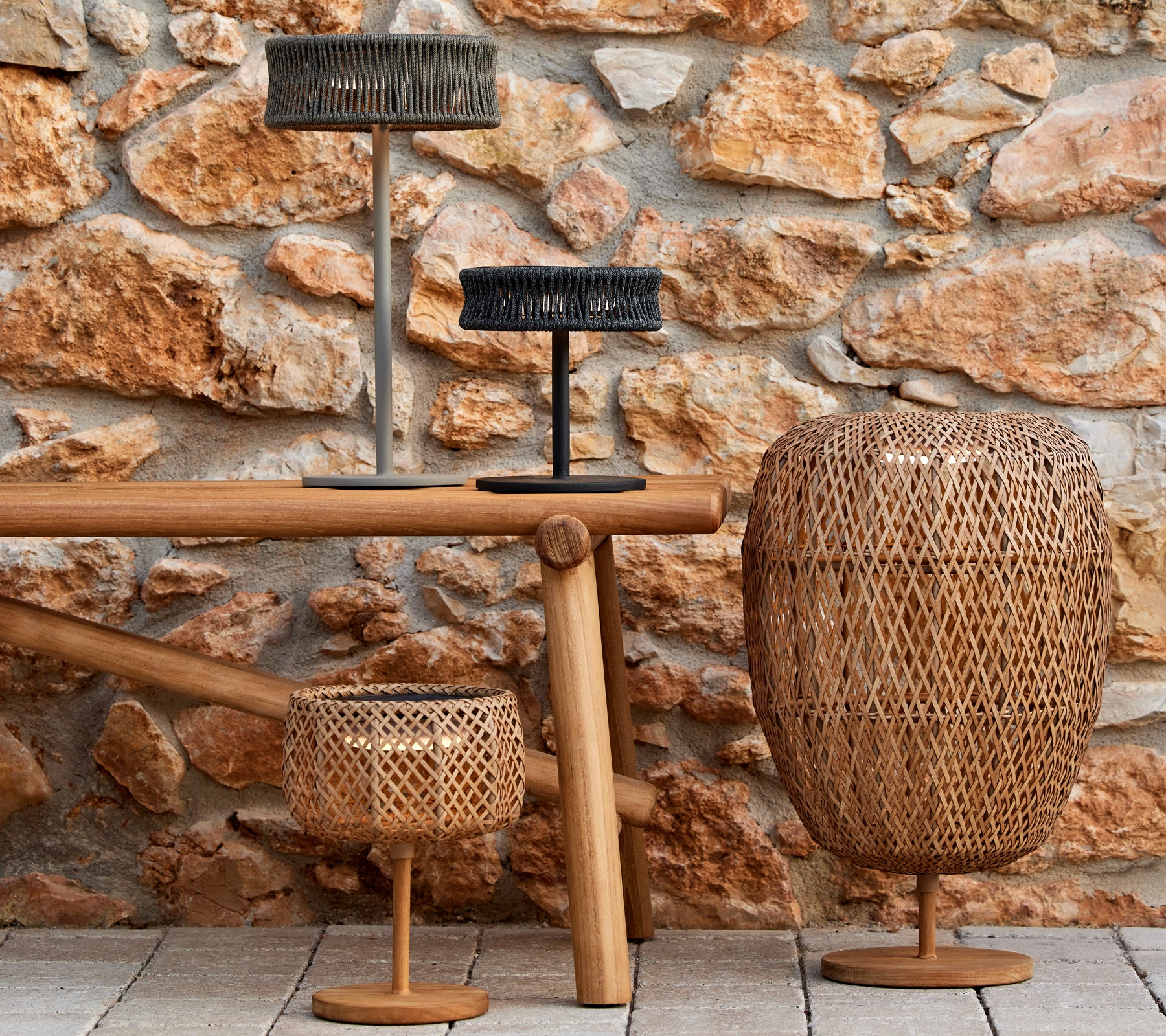 Three decorative lamps in varied shapes and sizes on a wooden table, set against a textured stone wall.