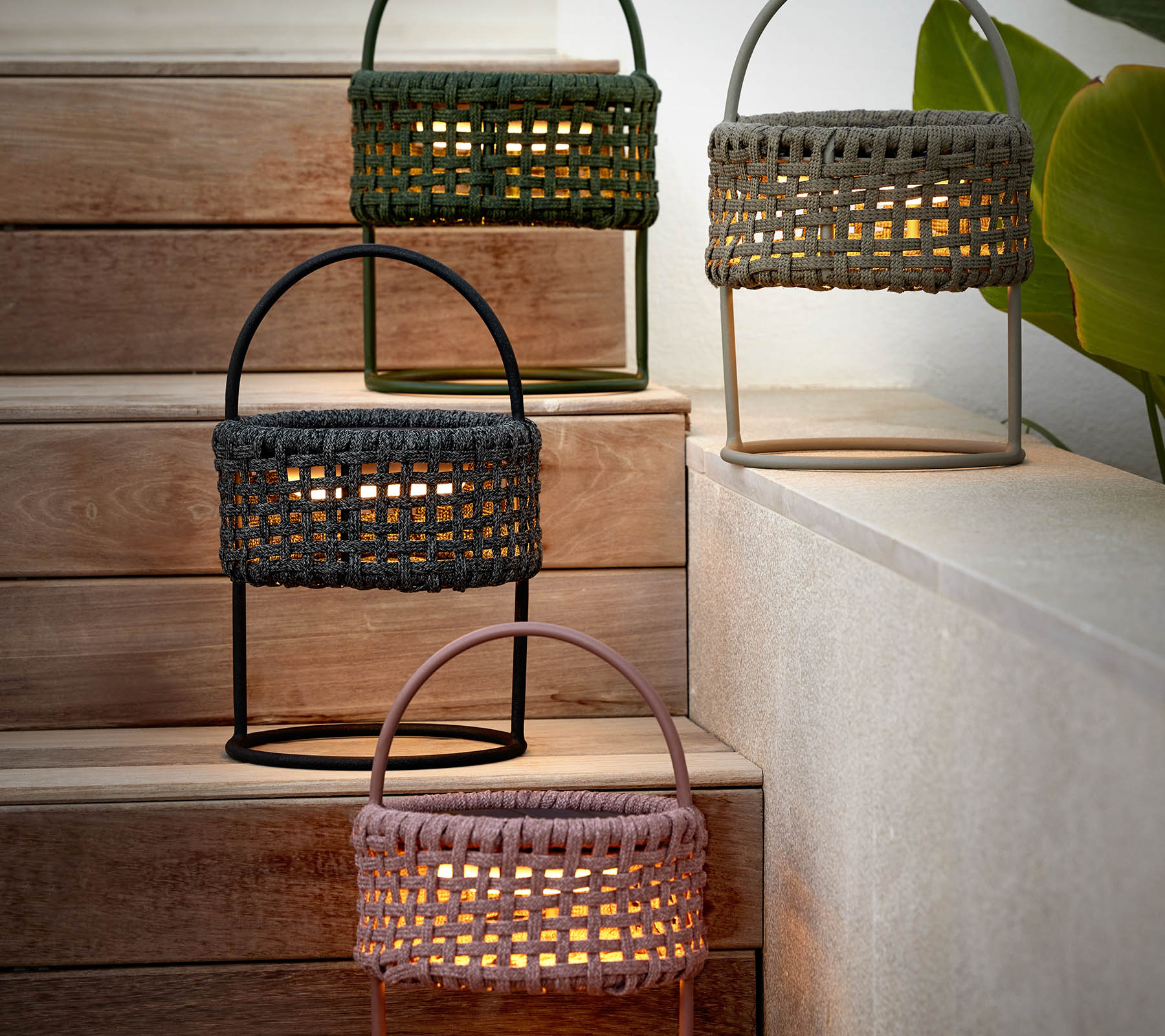 Three woven illusion lamps in various colors arranged on steps, casting a warm glow and adding a cozy ambiance to the setting.