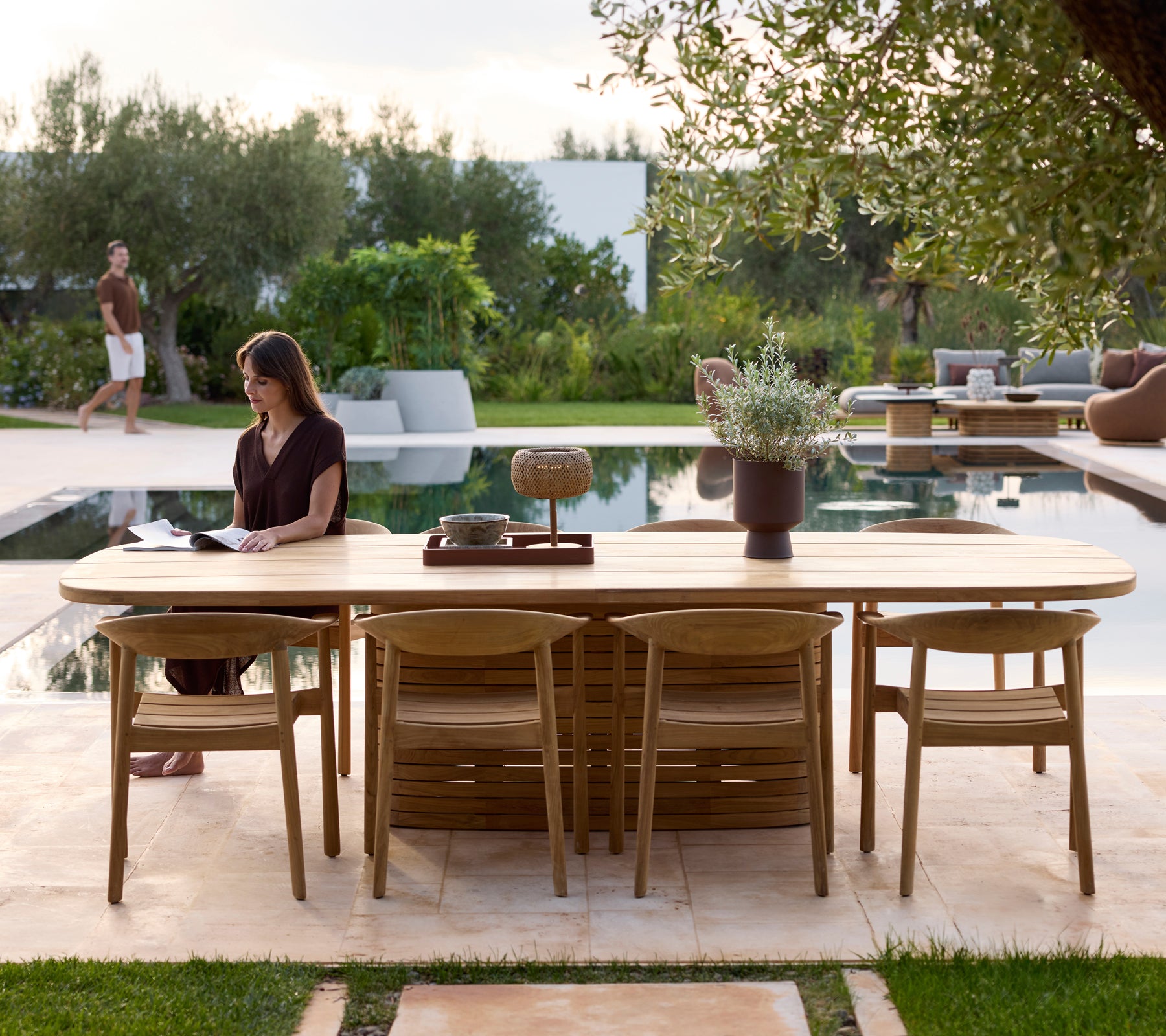 Modern outdoor table with chairs beside a pool surrounded by greenery.