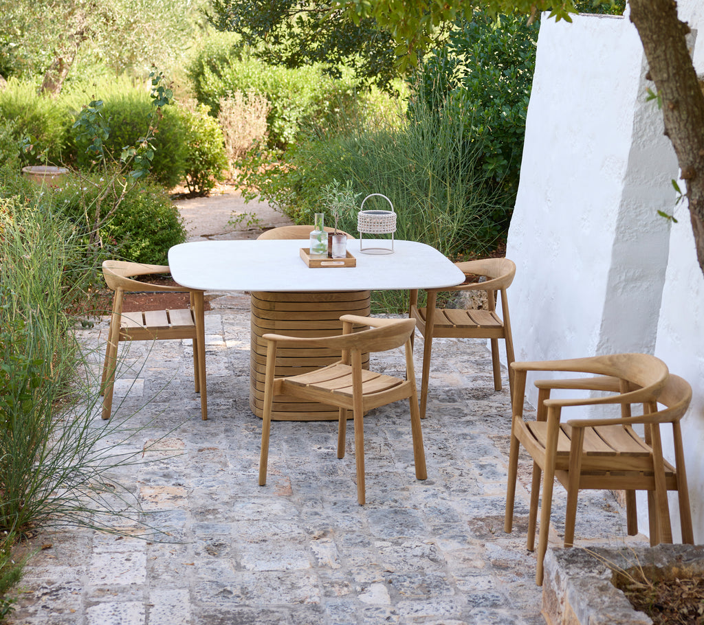 Modern outdoor setting with a white table and wooden chairs among greenery.
