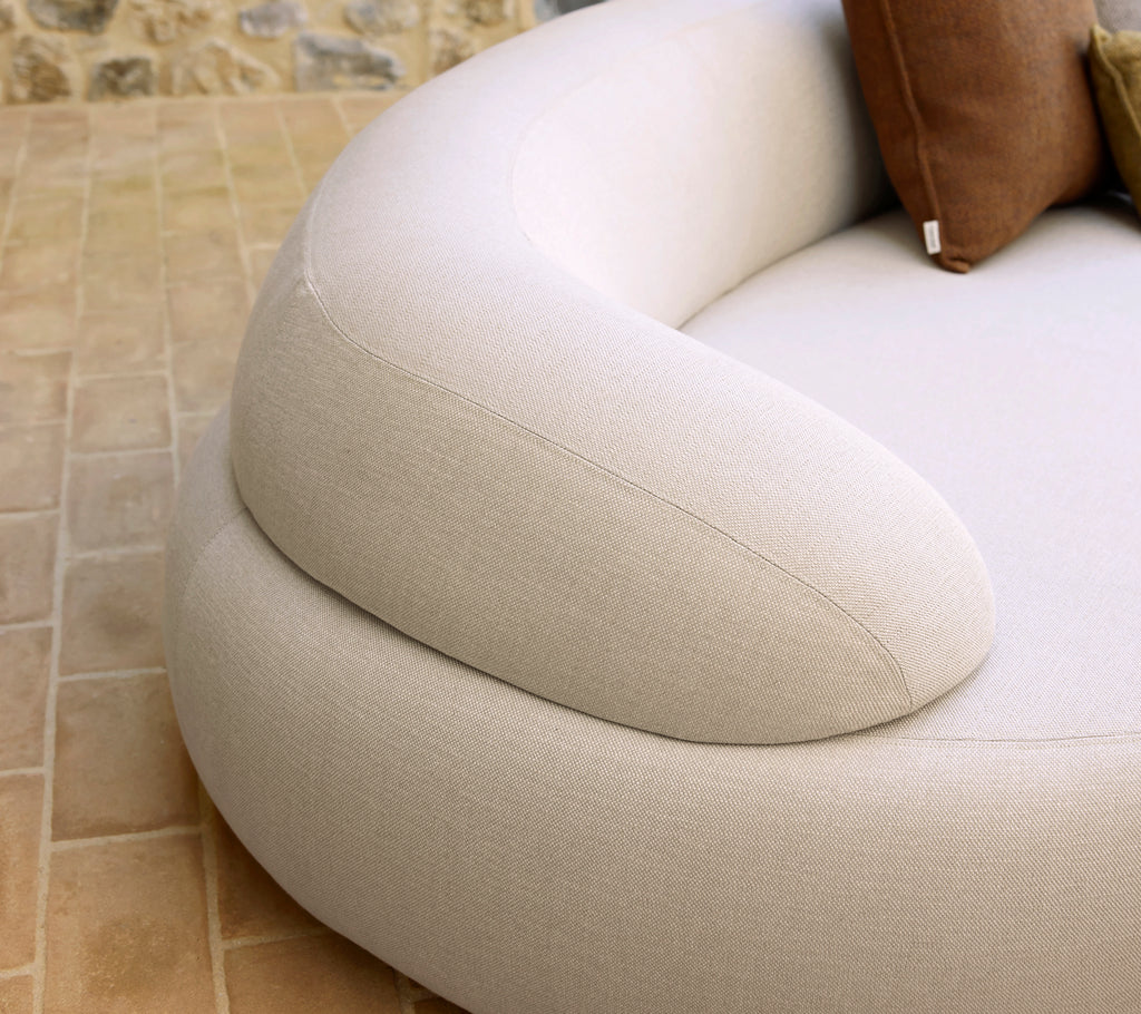 Soft, rounded armrest of a cozy seating piece, featuring a light fabric and complementary decorative pillows.