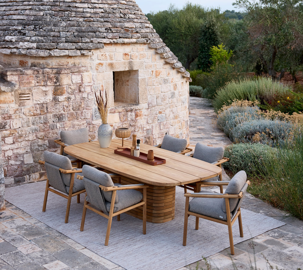 Wooden dining table with grey cushion chairs in a rustic outdoor setting.