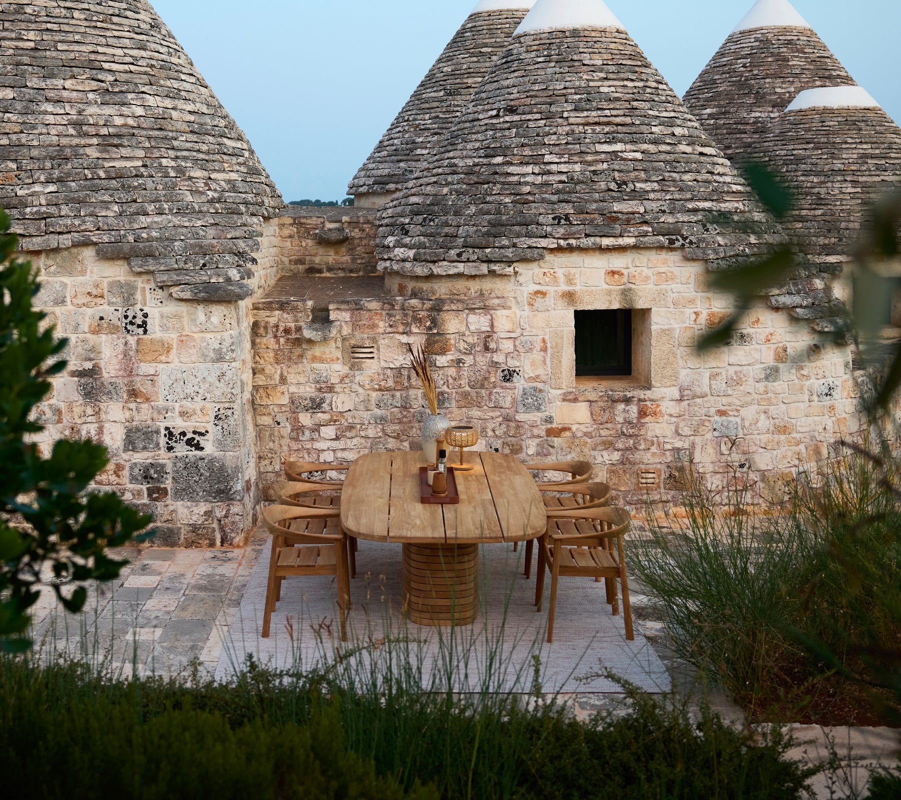 Wooden table with woven chairs set against a rustic stone backdrop.
