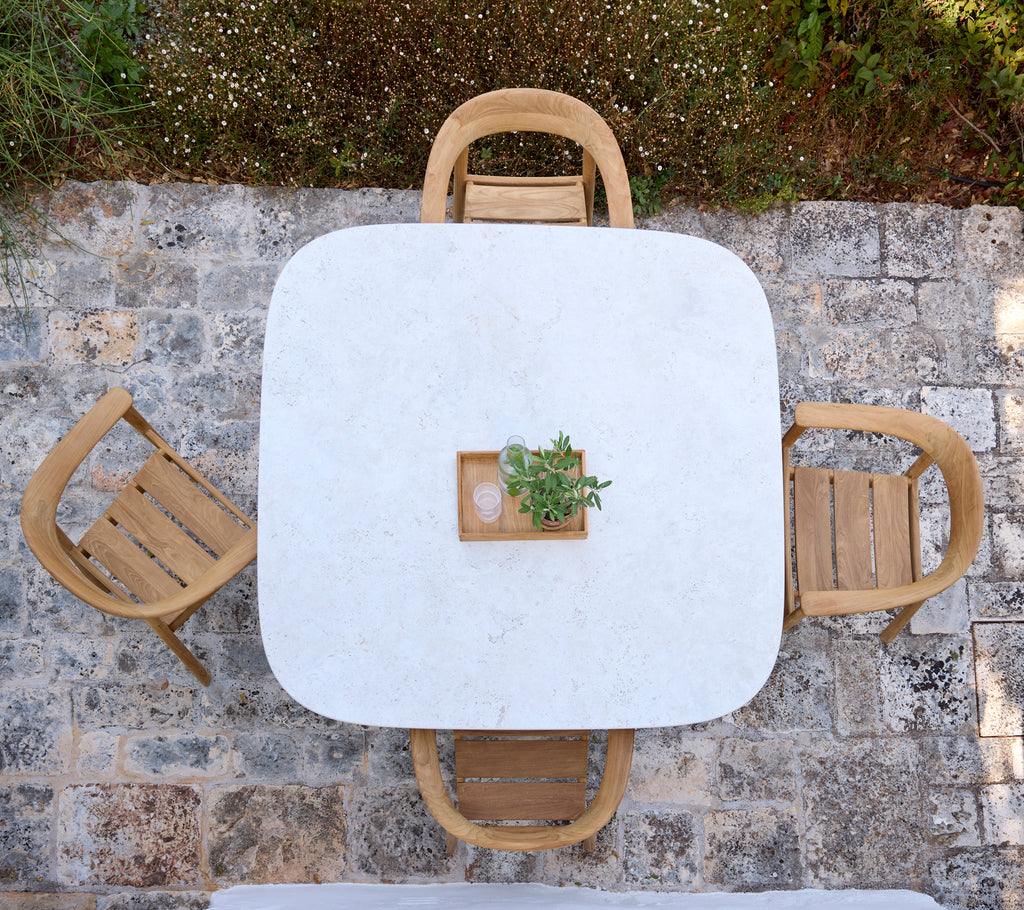 Modern white table with wooden chairs and a small plant centerpiece in an outdoor setting.
