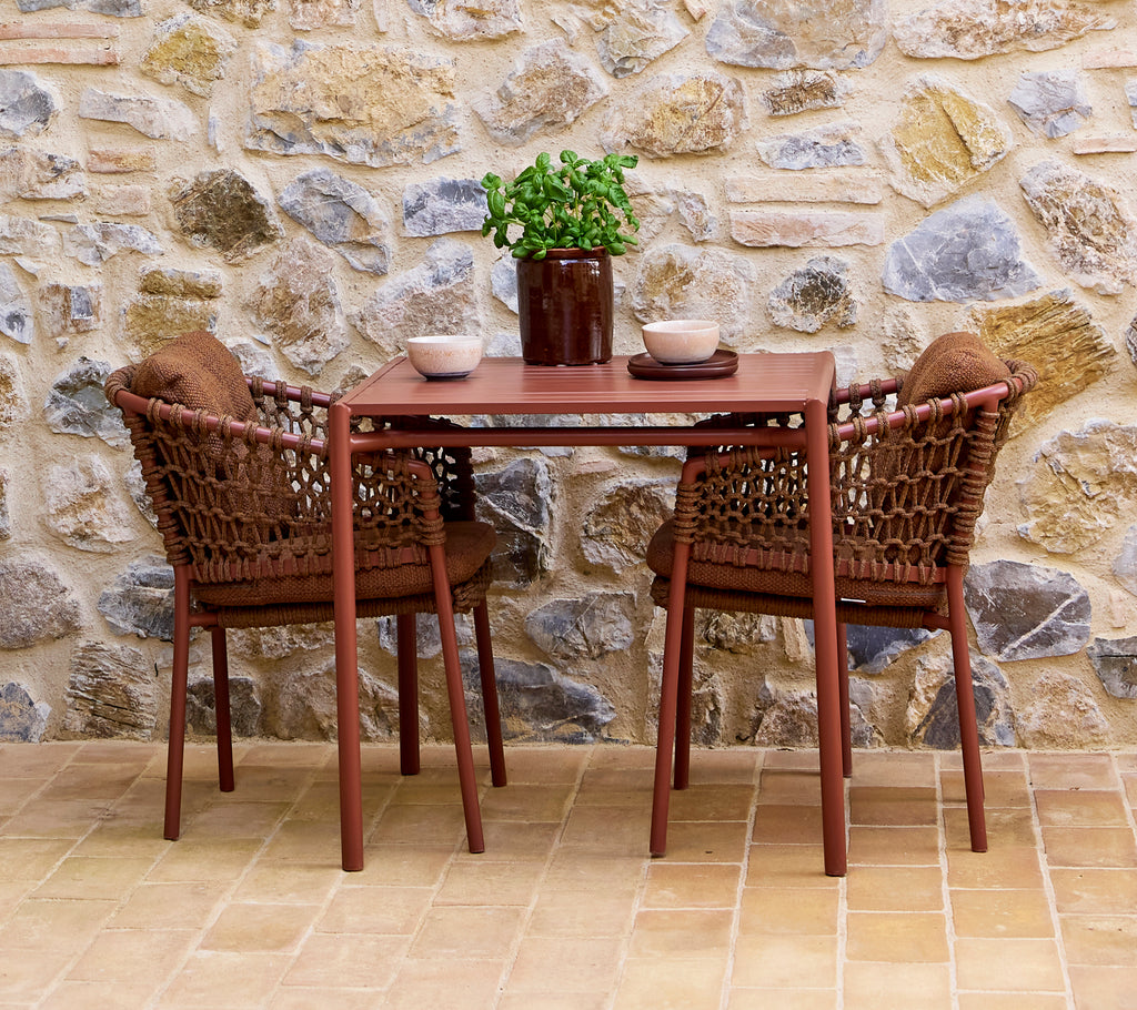 Brown umber chairs paired with a matching table, accented by a potted plant and decorative bowls, against a stone wall backdrop.
