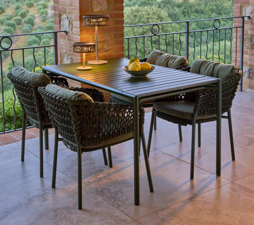 A stylish green Ocean dining chair set around a rectangular table, complemented by a decorative lamp and a bowl of fruit.