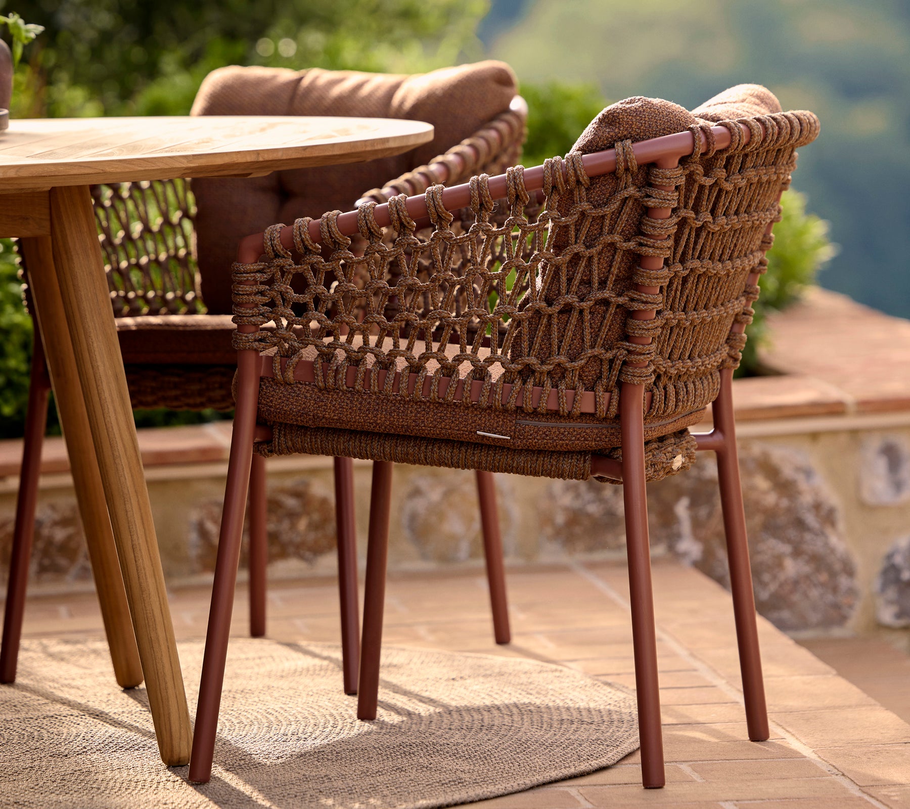 Umber brown dining chair featuring a woven design with sturdy legs, positioned next to a round table and surrounded by greenery.
