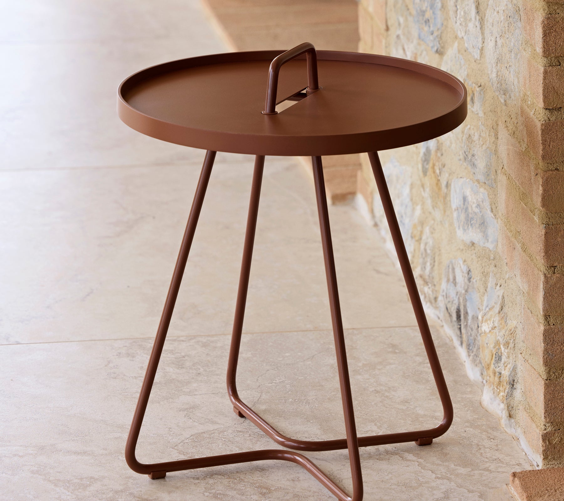 A round table in a desert red finish with a handle and three slender legs, designed for versatility and ease of movement.