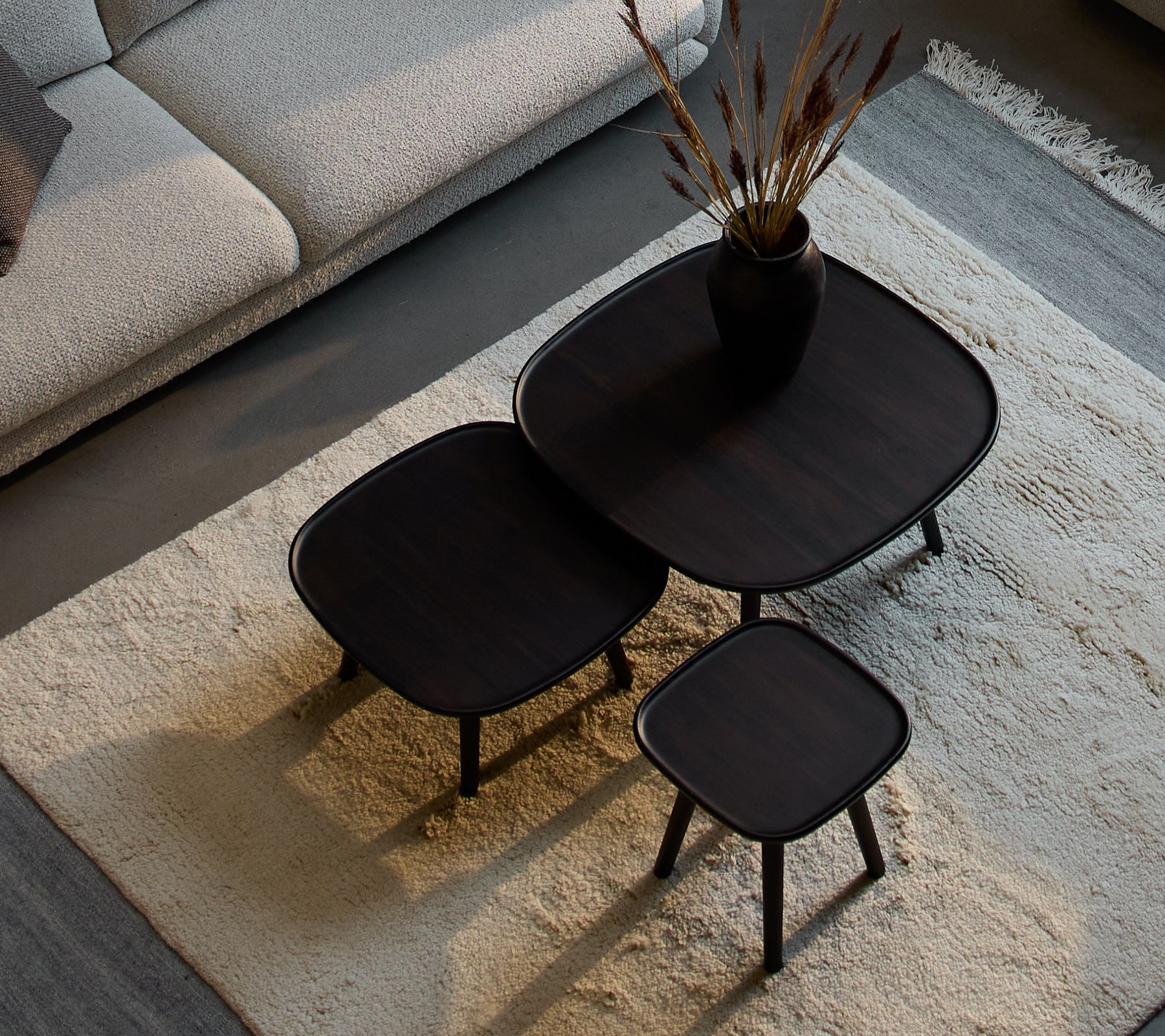 Three stylish Pace coffee tables in varying sizes, featuring a sleek design and dark finish, accompanied by a decorative vase and dried plants.