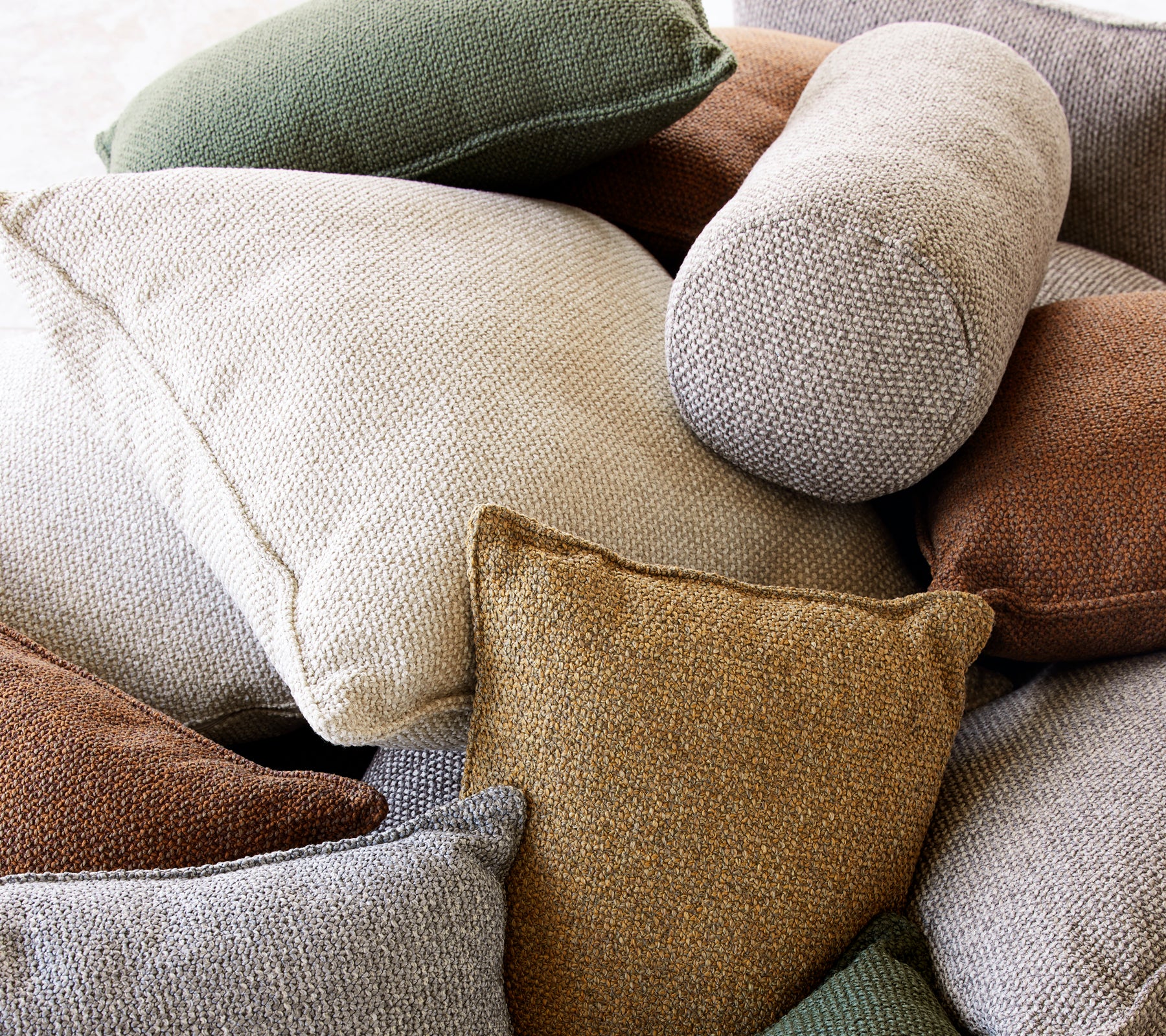 A variety of textured scatter cushions in neutral tones and earthy colors, showcasing diverse shapes and sizes.