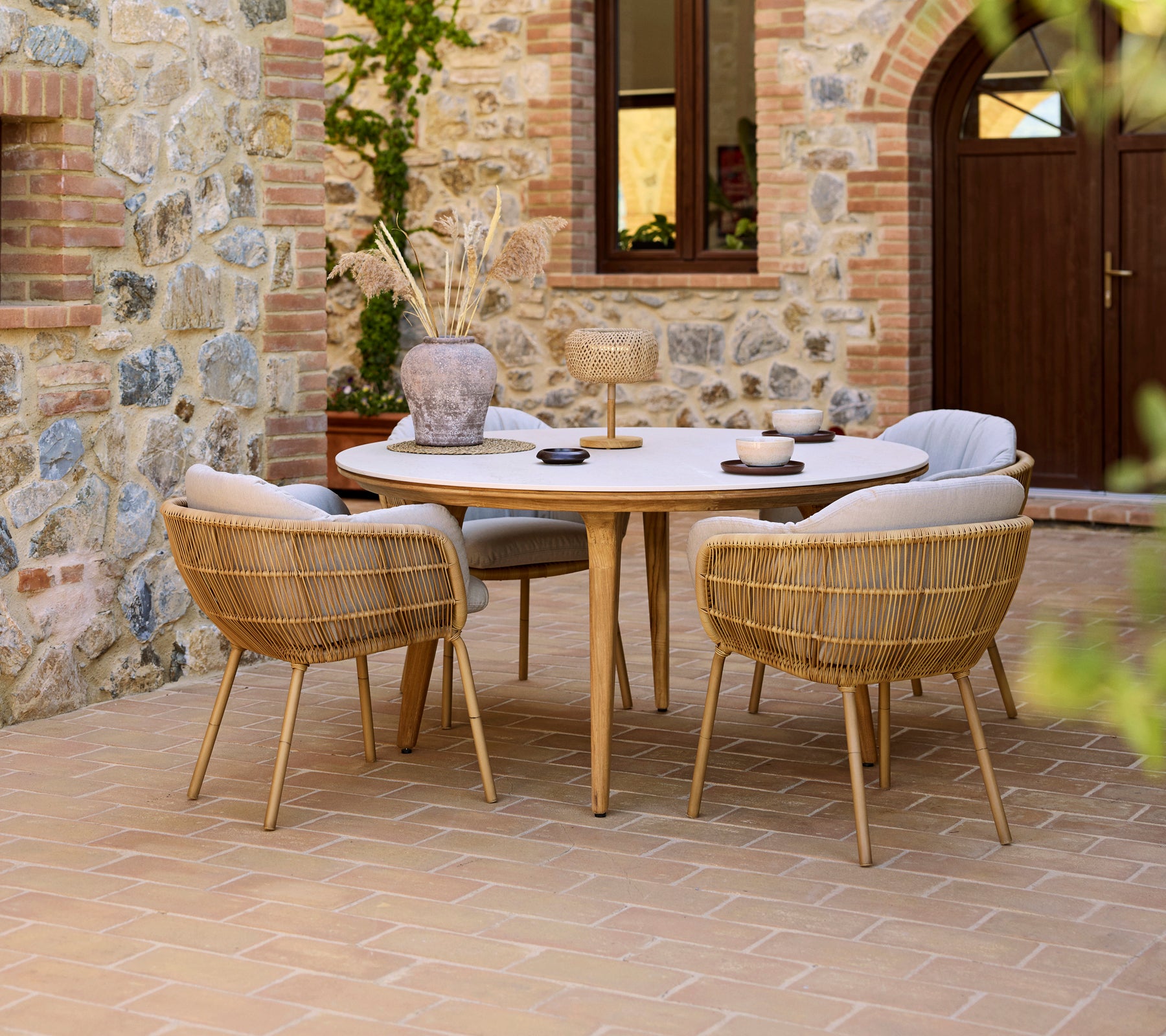 Outdoor dining setup featuring a round Aspect table with Stay chairs, set against a stone wall backdrop.