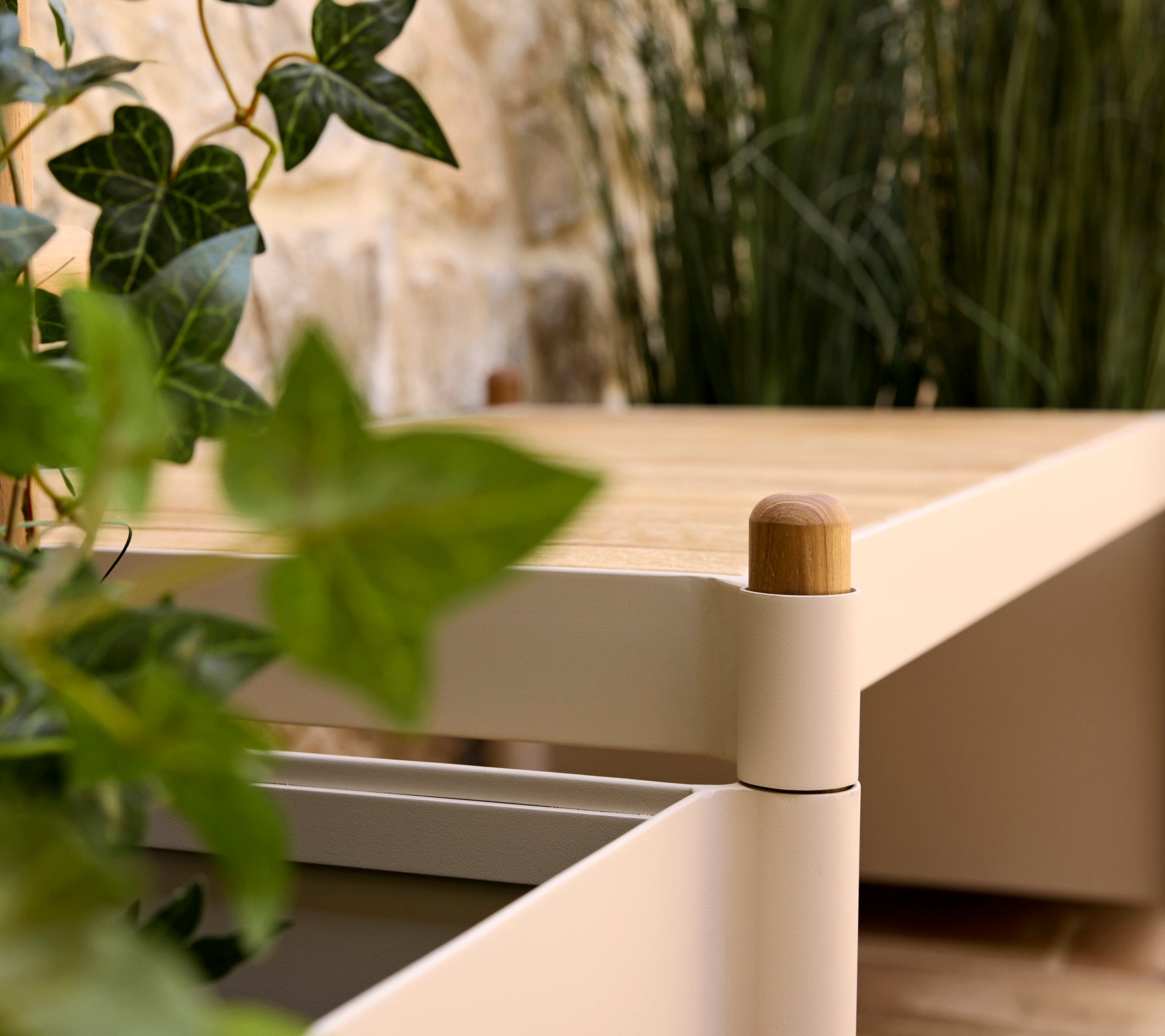 A stylish bench with a wooden top and soft edges, accompanied by greenery in a planter, enhancing a serene atmosphere.