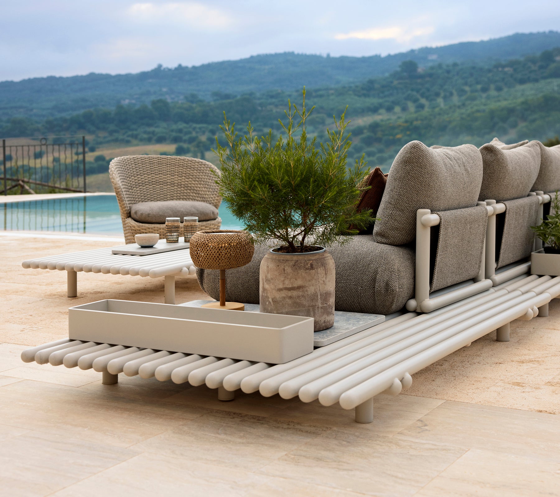 A stylish lounge area featuring a comfortable chair, a storage box, and an elegant sticks platform made of aluminum, surrounded by greenery.