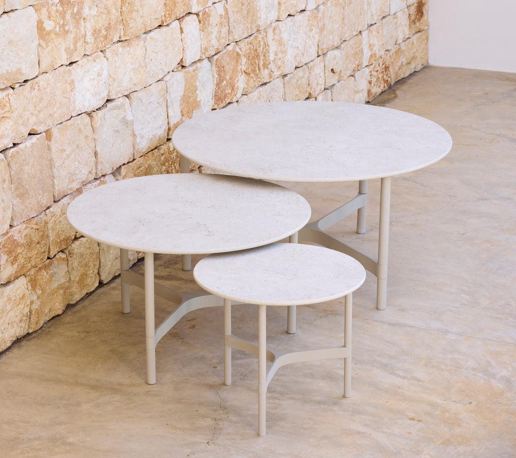 Three modern round tables in varying sizes against a stone wall.