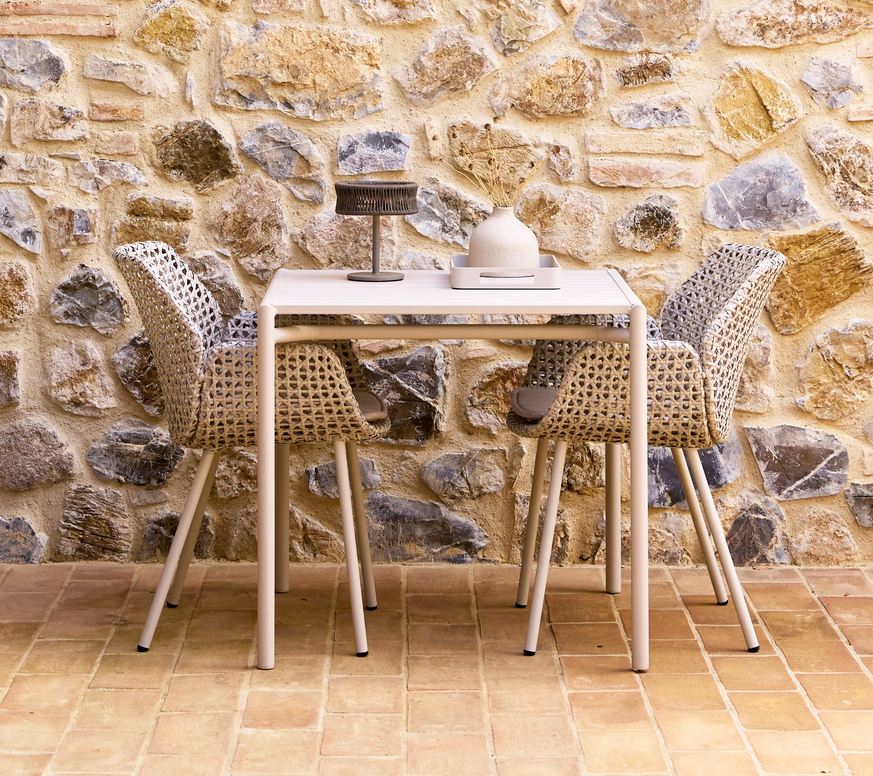 A stylish dining set featuring sand-colored vibe chairs arranged around a modern table, set against a textured stone wall.