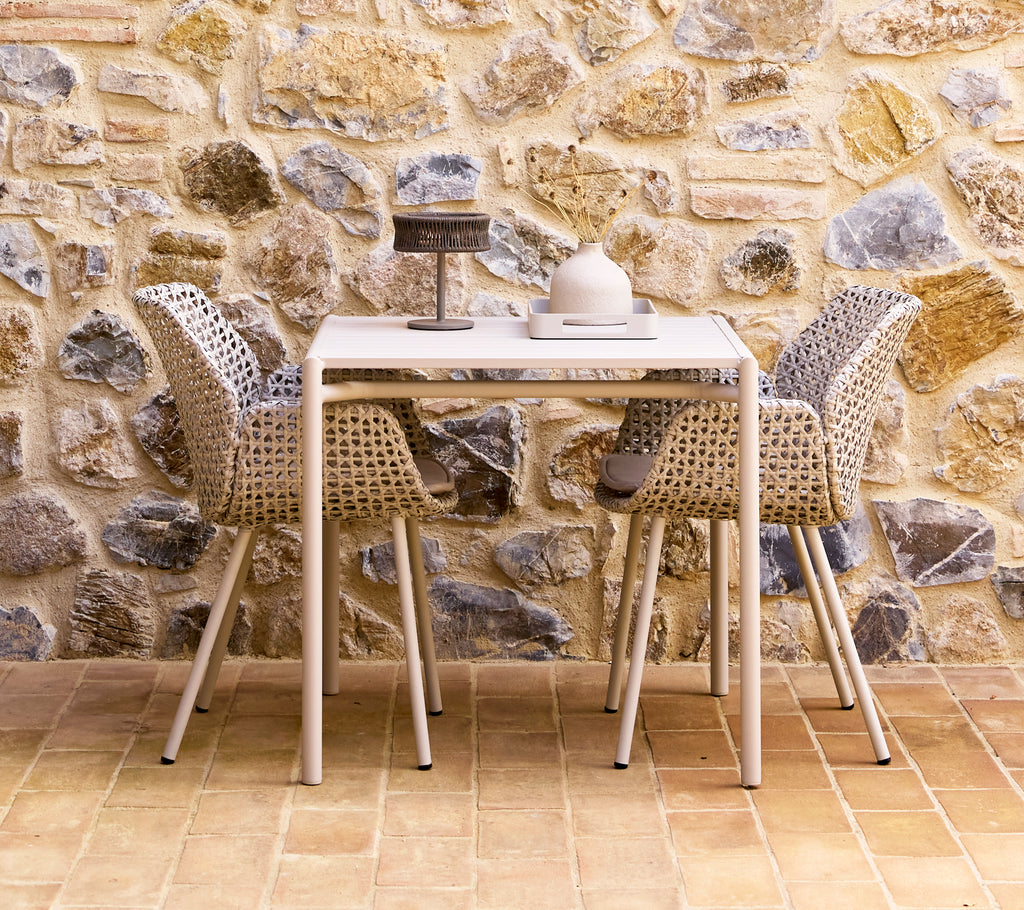A stylish dining set featuring sand-colored vibe chairs arranged around a modern table, set against a textured stone wall.